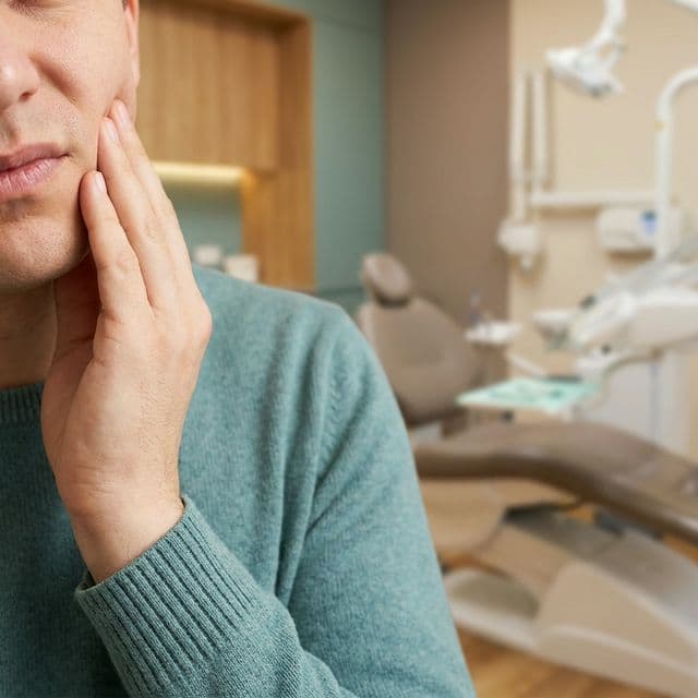 Person holding their jaw in discomfort at a dental office